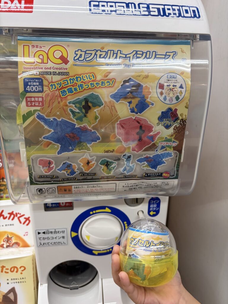 LaQ恐竜カプセルトイで出た黄色いカプセルをガチャガチャ本体の前で持っている様子